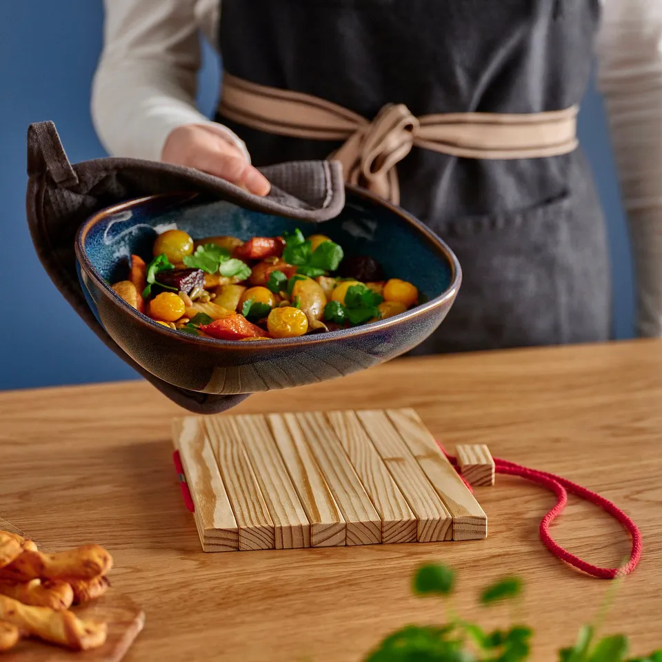 Chef holds colourful veggie bowl on wooden stand.