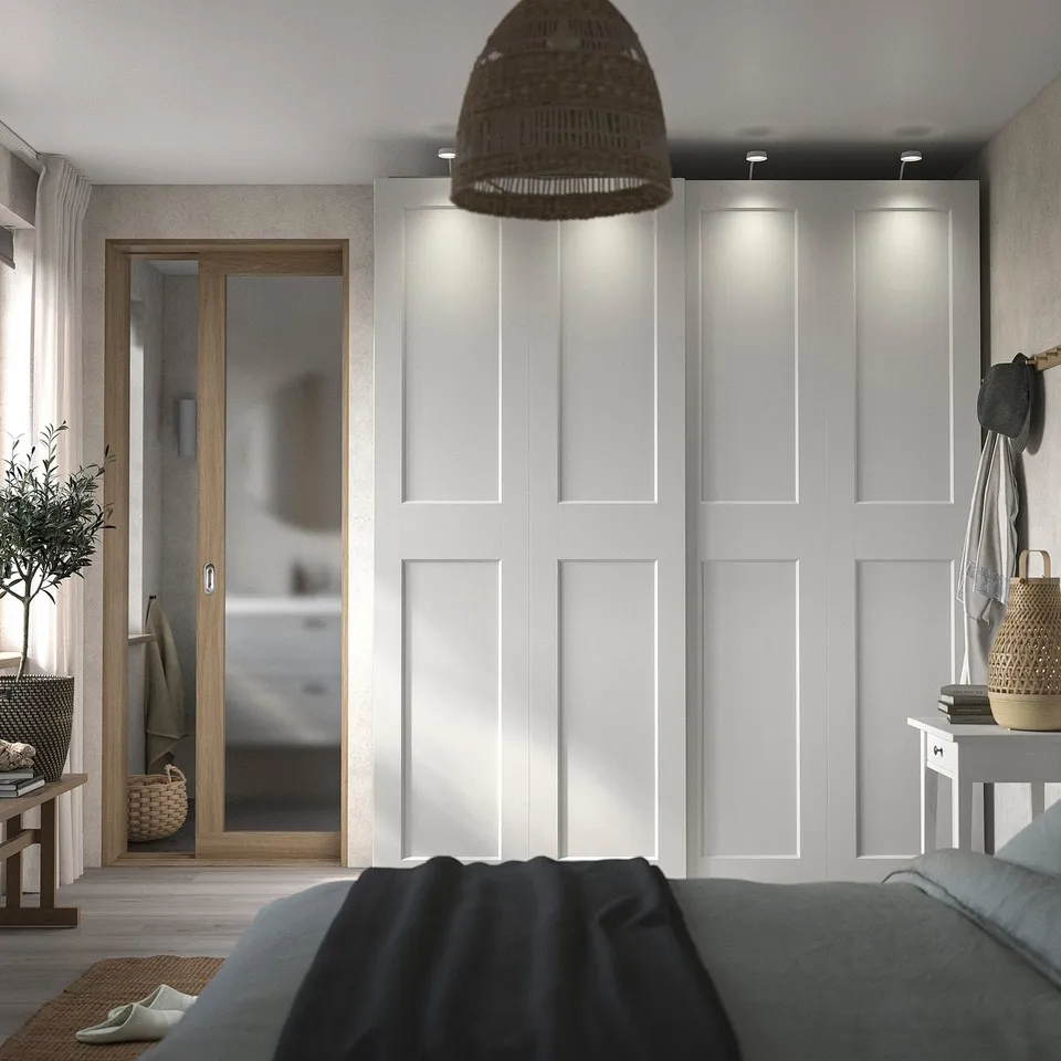 Modern bedroom with white built-in wardrobe, grey bed, wooden door, and wicker lamp.