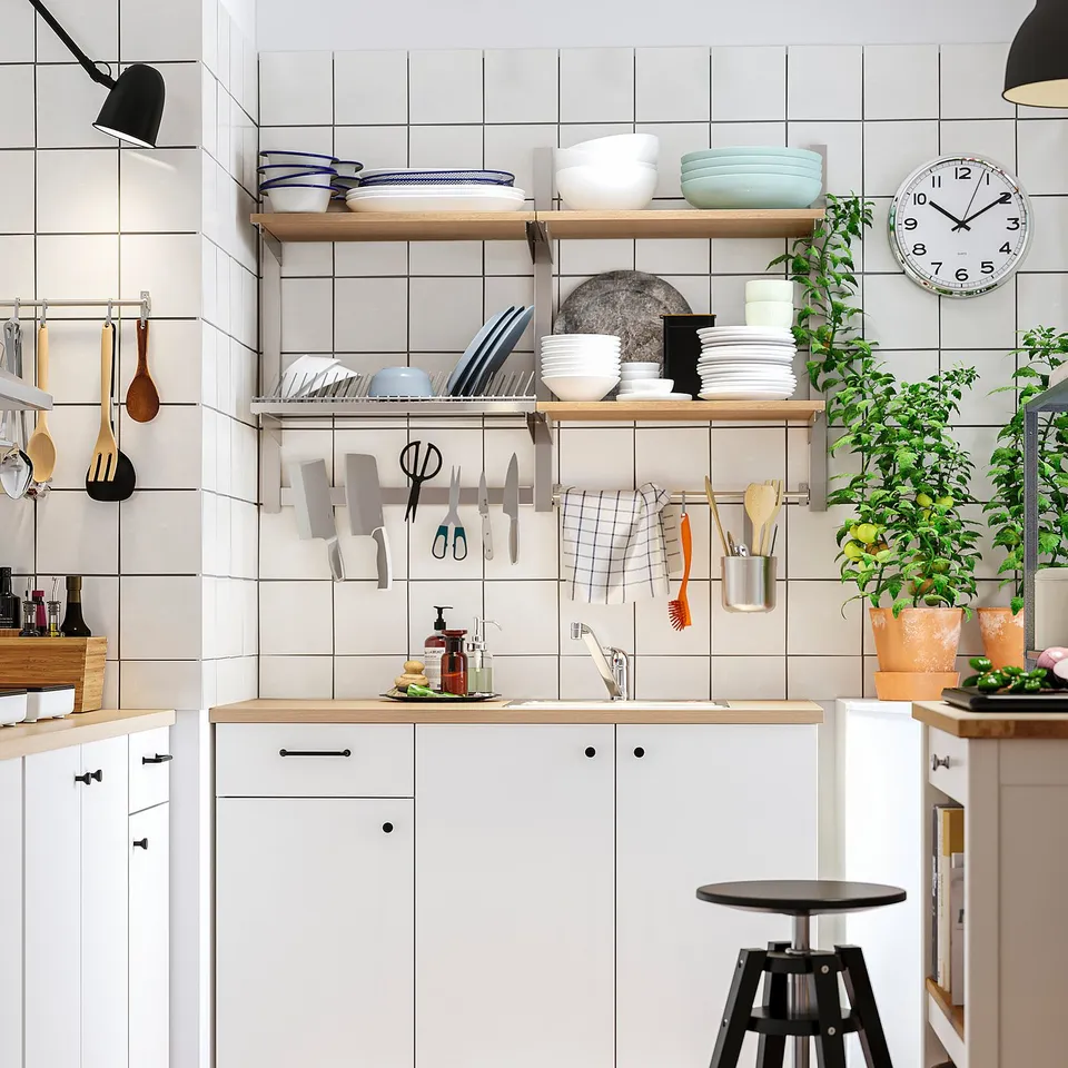 Modern kitchen with KUNGSFORS wall storage, stacked plates, hanging knives, plant, stool, black lamps, wooden counter, and clock.