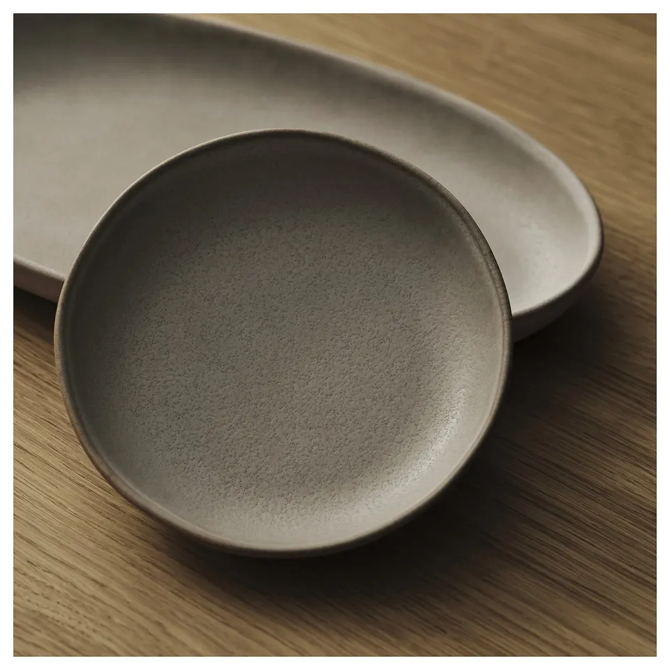 Rustic serving plates, grey stoneware, round & oval shapes, resting on wooden surface.