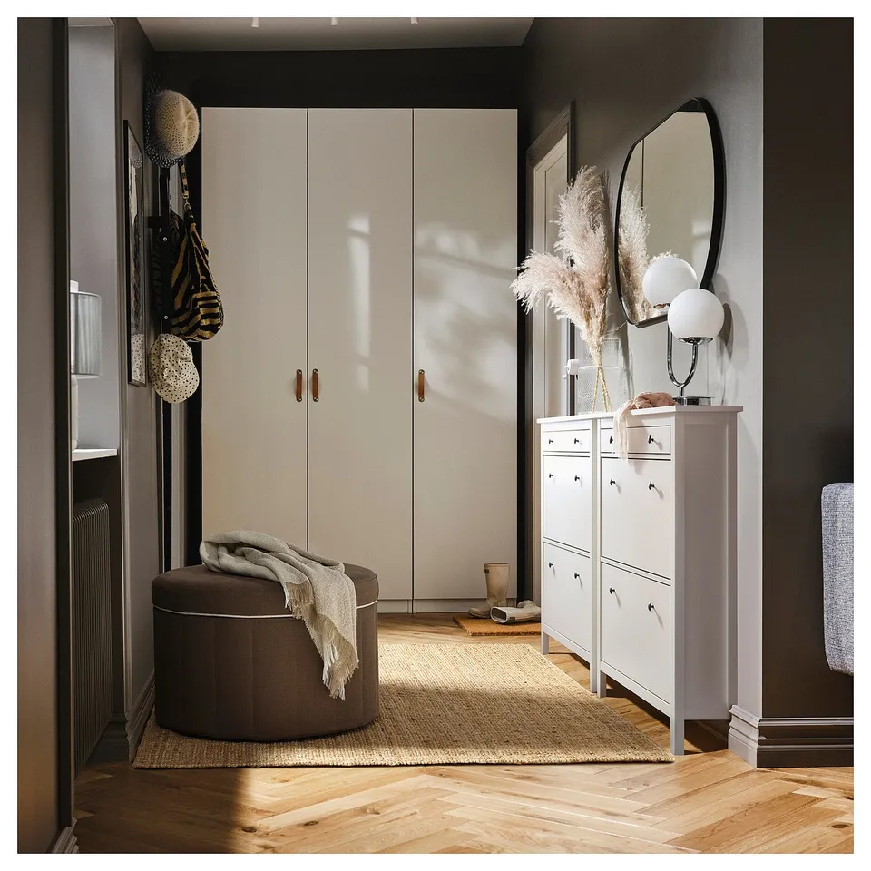 Well-organized entryway with a large off-white wardrobe, round brown storage ottoman, white shoe cabinet, and decorative mirror and plants.