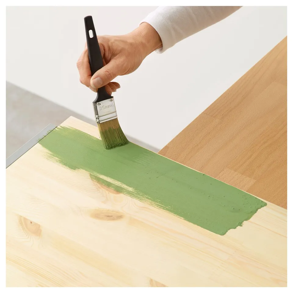 Person painting wooden surface with green paint using TRIXIG brush, showing smooth application.