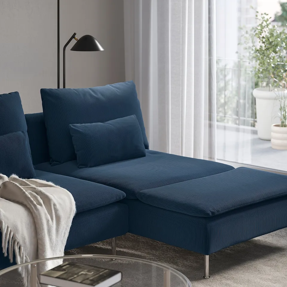 Blue sofa with pillows by a big window, chaise lounge, floor lamp, cosy room.