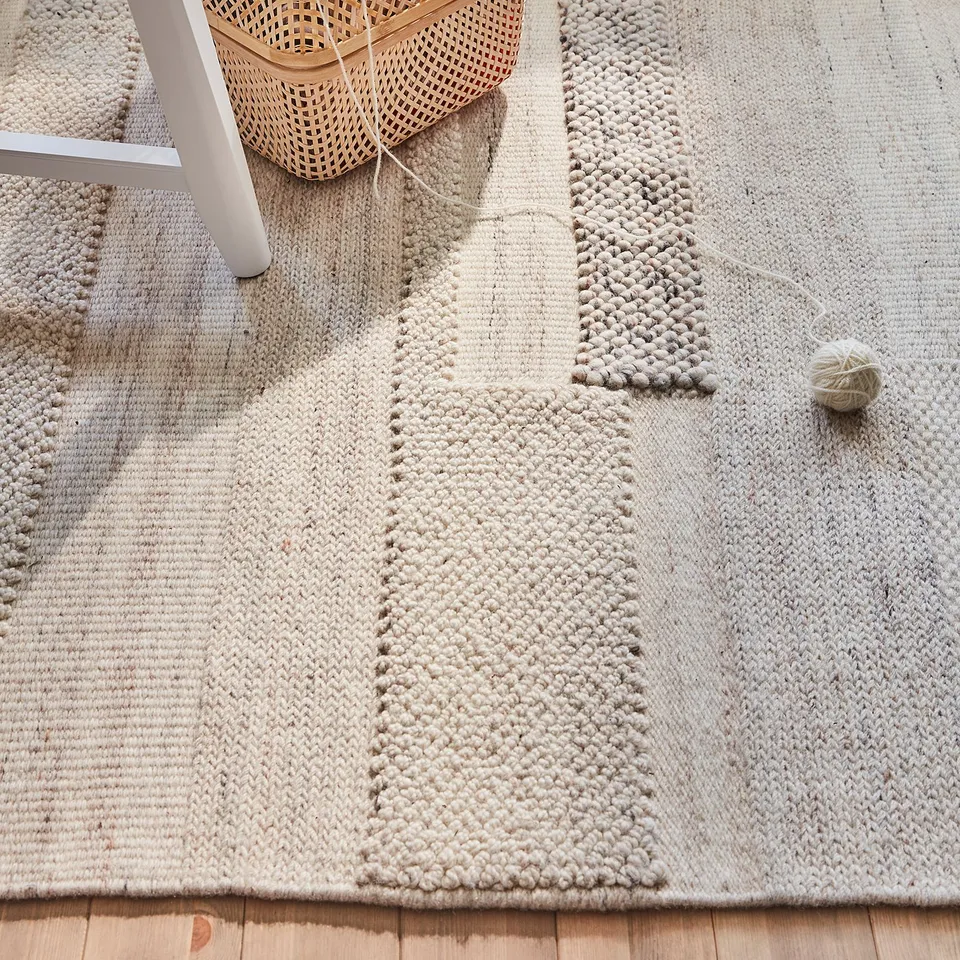BRÖNDEN neutral woven rug on wooden floor with basket.