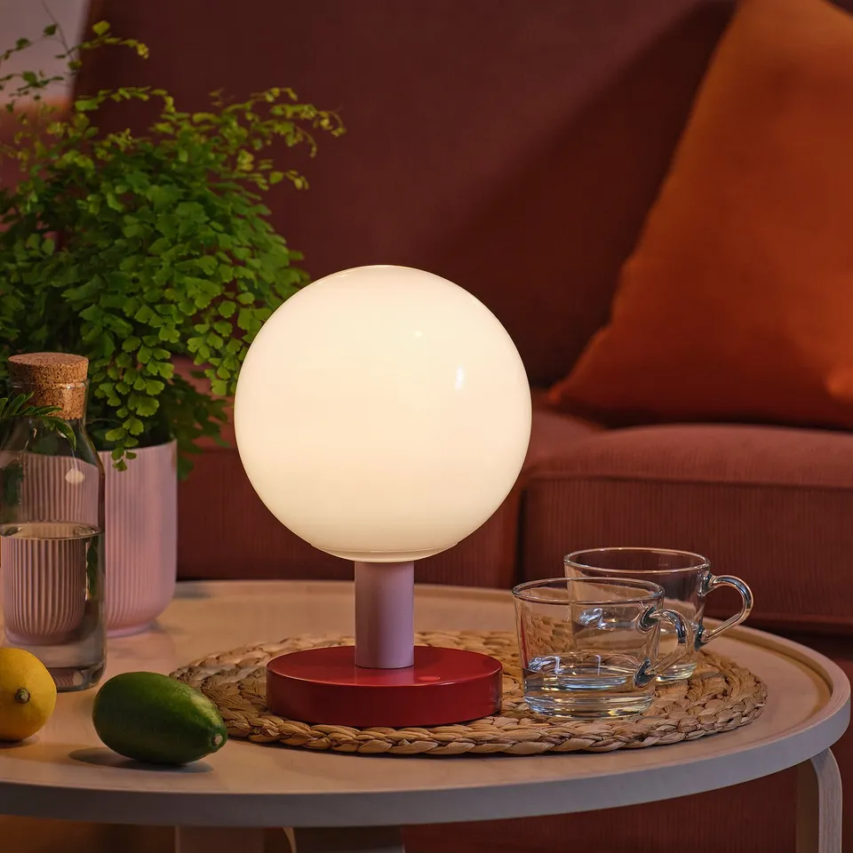 Round lamp on table with cups and fruit. Soft light illuminates cosy setting.