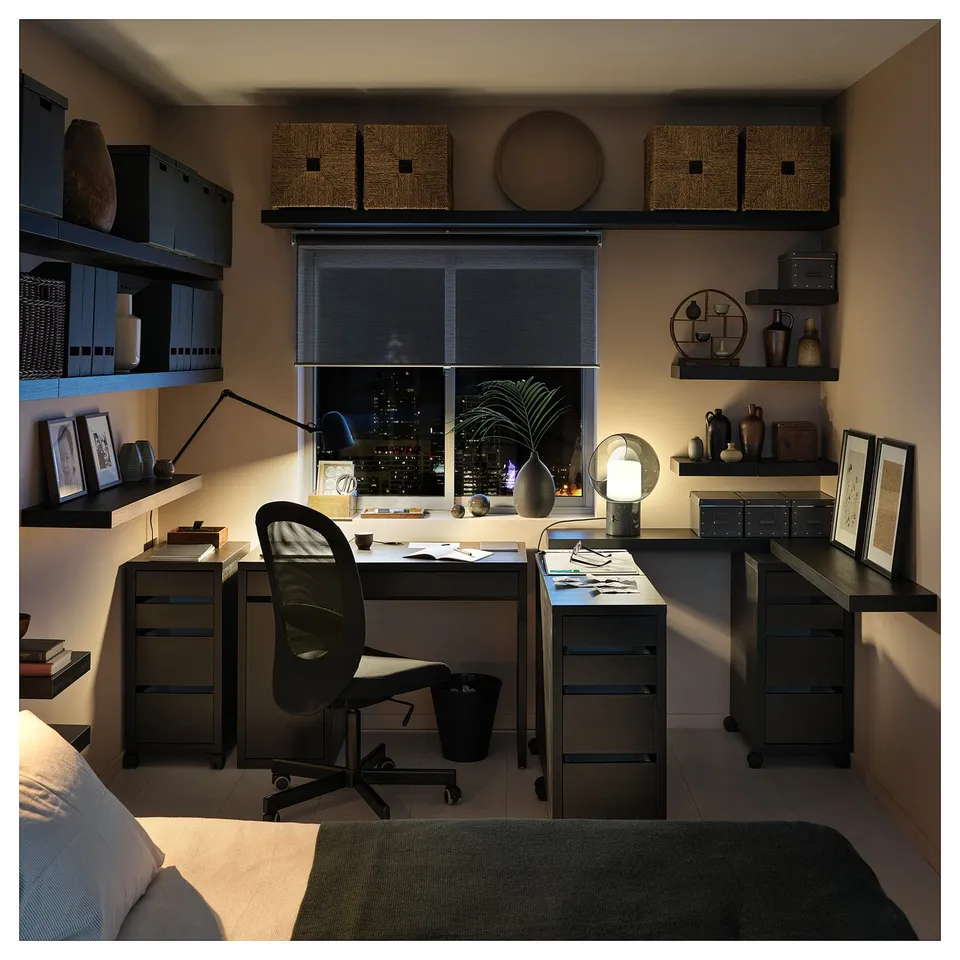 Modern home office with black MICKE desk, chair, and shelves. Decorated with plants, lamps, and vases. Night view with window city lights.
