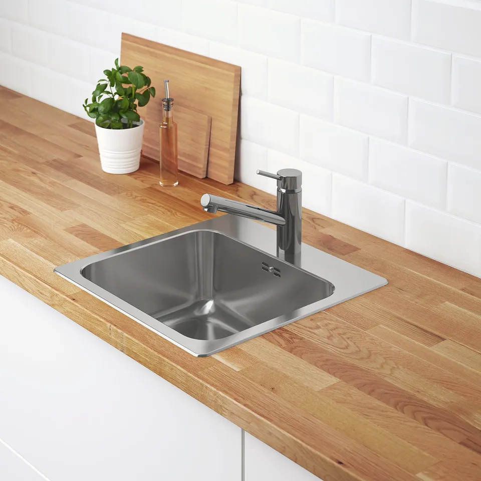 Stainless steel sink inset in timber countertop. Chrome tap. White brick backsplash. Wooden cutting boards and green potted plant on counter.