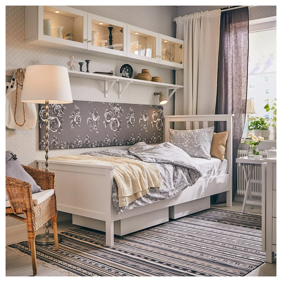 Cosy bedroom with white HEMNES bed, floral headboard, wicker chair, and stripe rug.