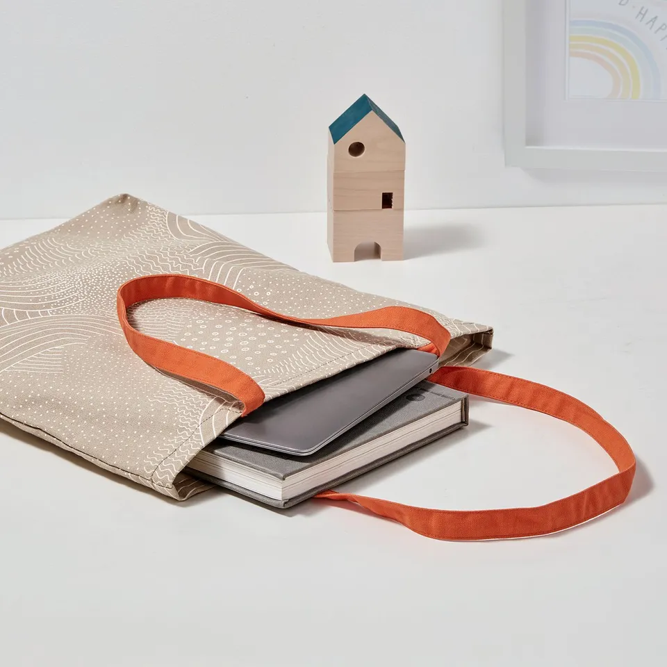 Beige tote bag with orange handles, white pattern, for laptop & papers.
