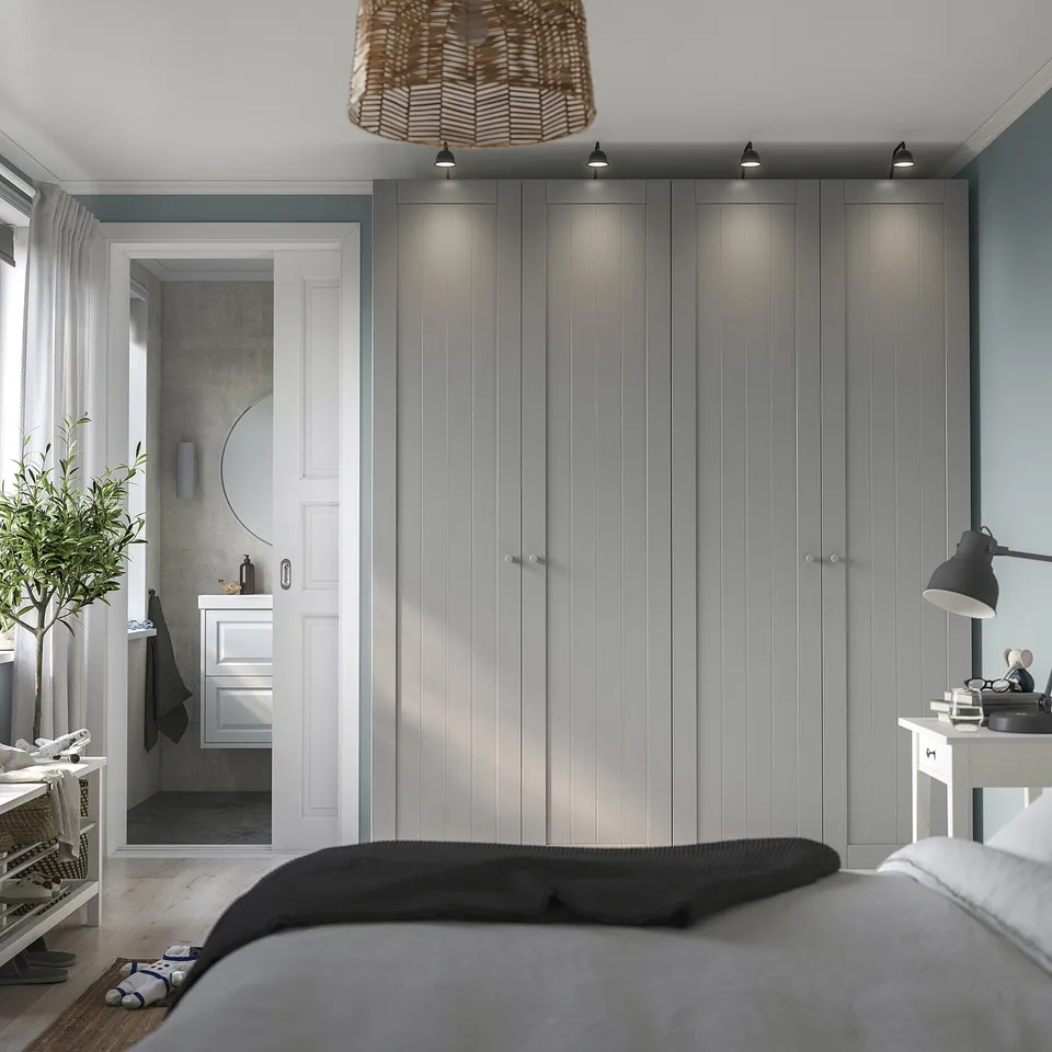 Modern grey GULLABERG wardrobes beside a bathroom door, beside a bed with dark blanket.