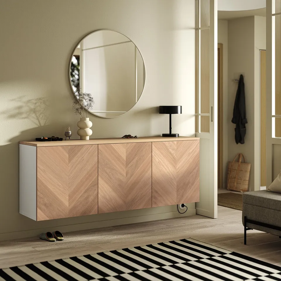 KVALMSÖ mirror, light frame, above wooden cabinet with lamp and dried flowers. Rug, coats, shoes, bag by entry.