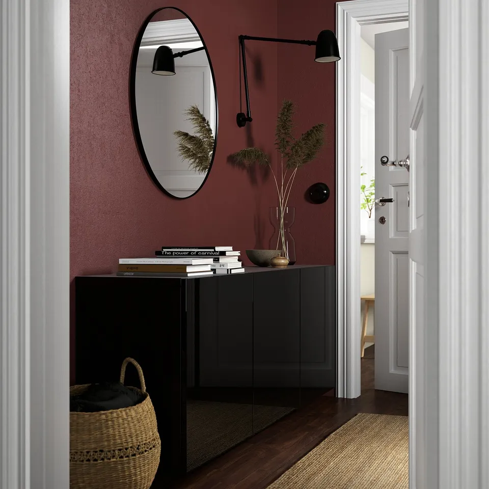 Black BESTÅ sideboard with books, plant, bowl, mirror, basket, and sconces against burgundy wall.