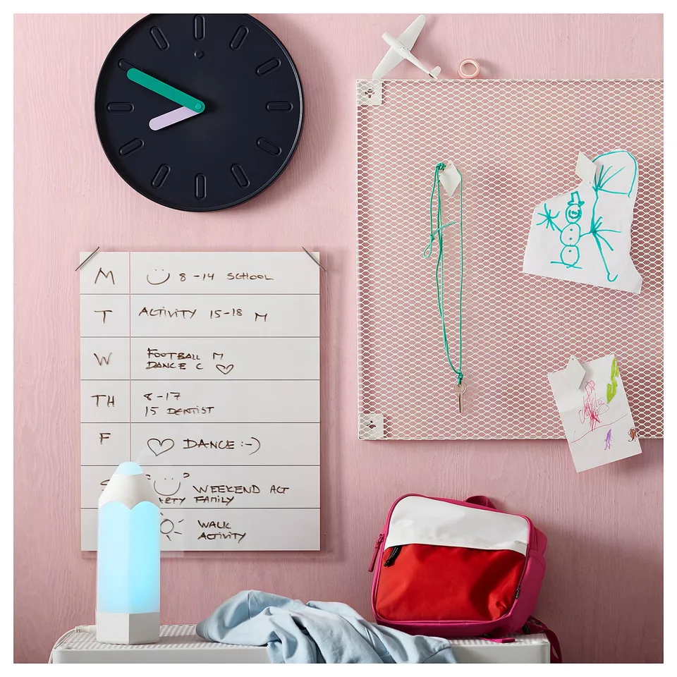 Organised kids room with red backpack, playful clock, whiteboard schedule, mesh pinboard with drawings, and a colourful nightlight named PELARBOJ.