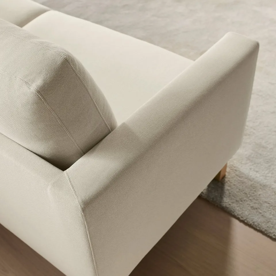 Clean, modern sofa with light fabric, square arms, and visible wooden legs, suggesting high-quality comfort and airy design.