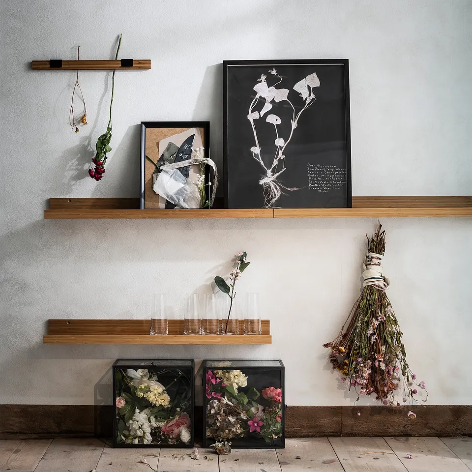 Wall shelf with framed art, dried flowers, and clear vases. Modern, minimalist design with natural wood.