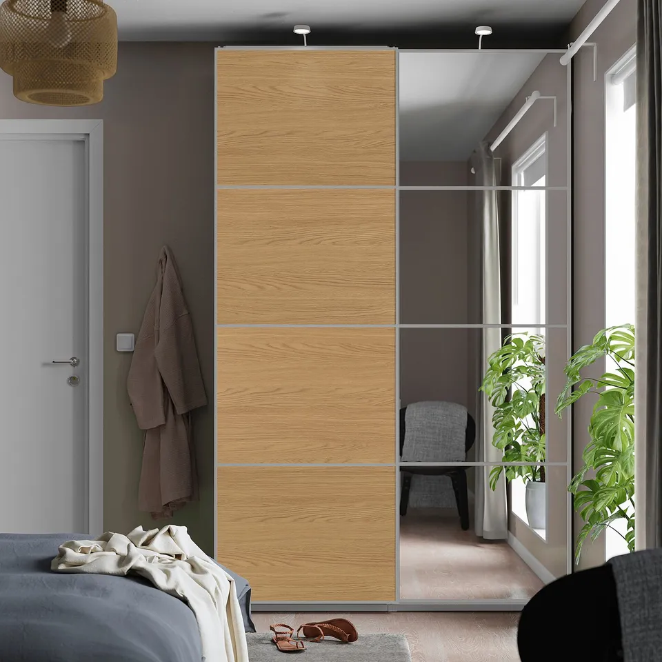Modern bedroom with a large mirrored wardrobe and a bed with a grey blanket and brown cloth.