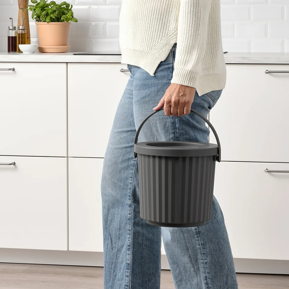 Person holding DAMMÄNG bin with lid, perfect for small waste like light bulbs.