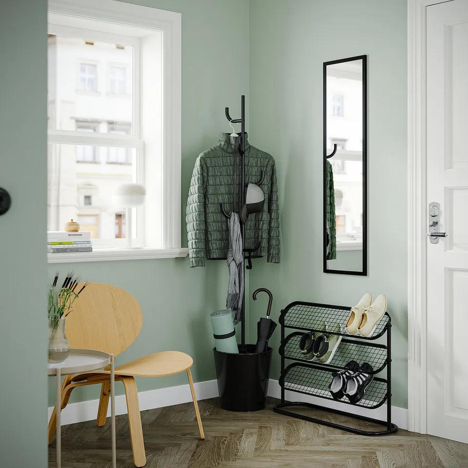 Modern entryway with light wood chair, green walls, black shoe rack, coat stand, and mirror.