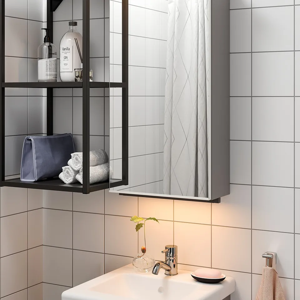 Modern bathroom with illuminated mirror and glass shelf, showcasing neatly rolled towels and toiletries.