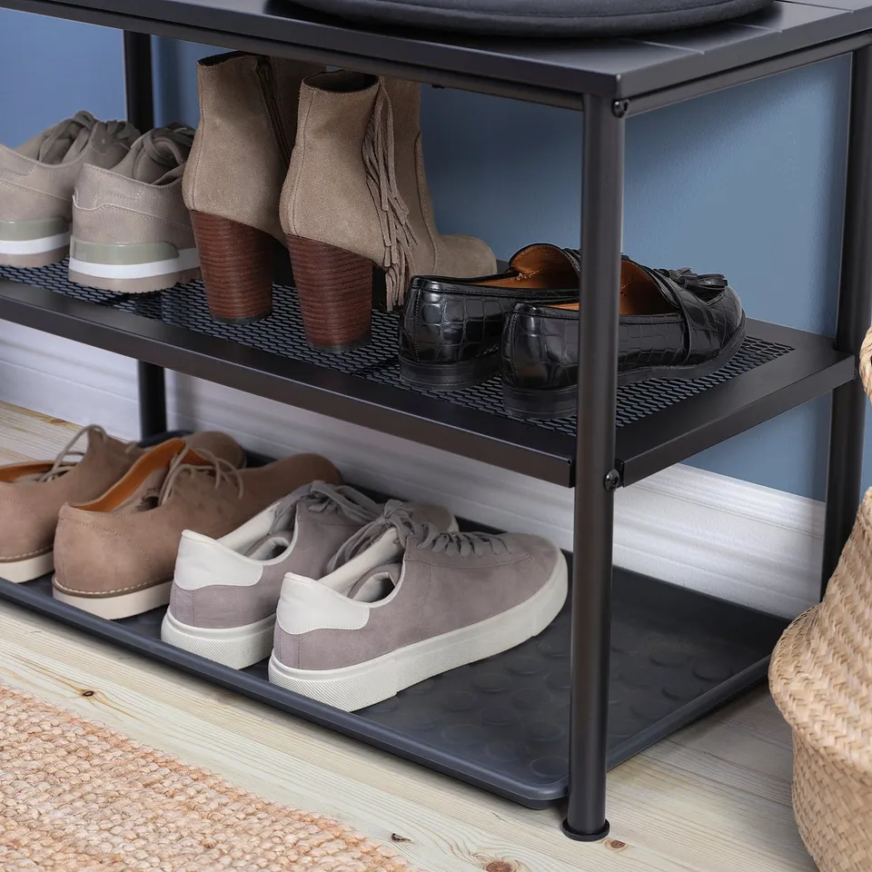 Three-tiered black metal shoe rack, holding assorted footwear on wooden floor.
