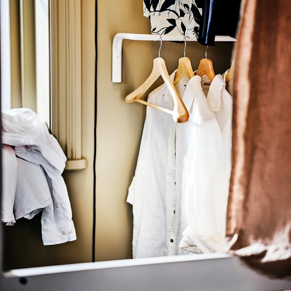 Closet with white hangers holding clothes. Light-colored jacket left, three white shirts middle, patterned shirt top, brown fabric right.