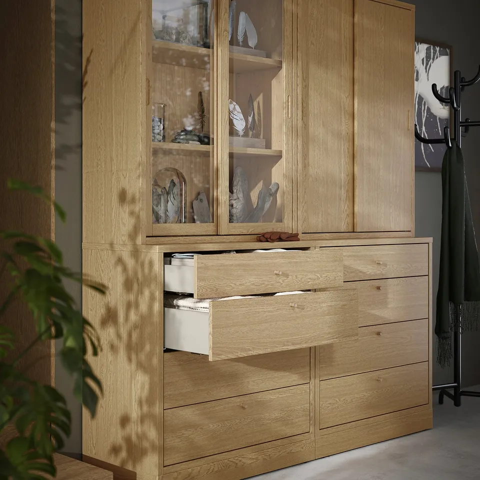 Wooden dresser with open drawer, cabinet, and glass doors displaying decor items.