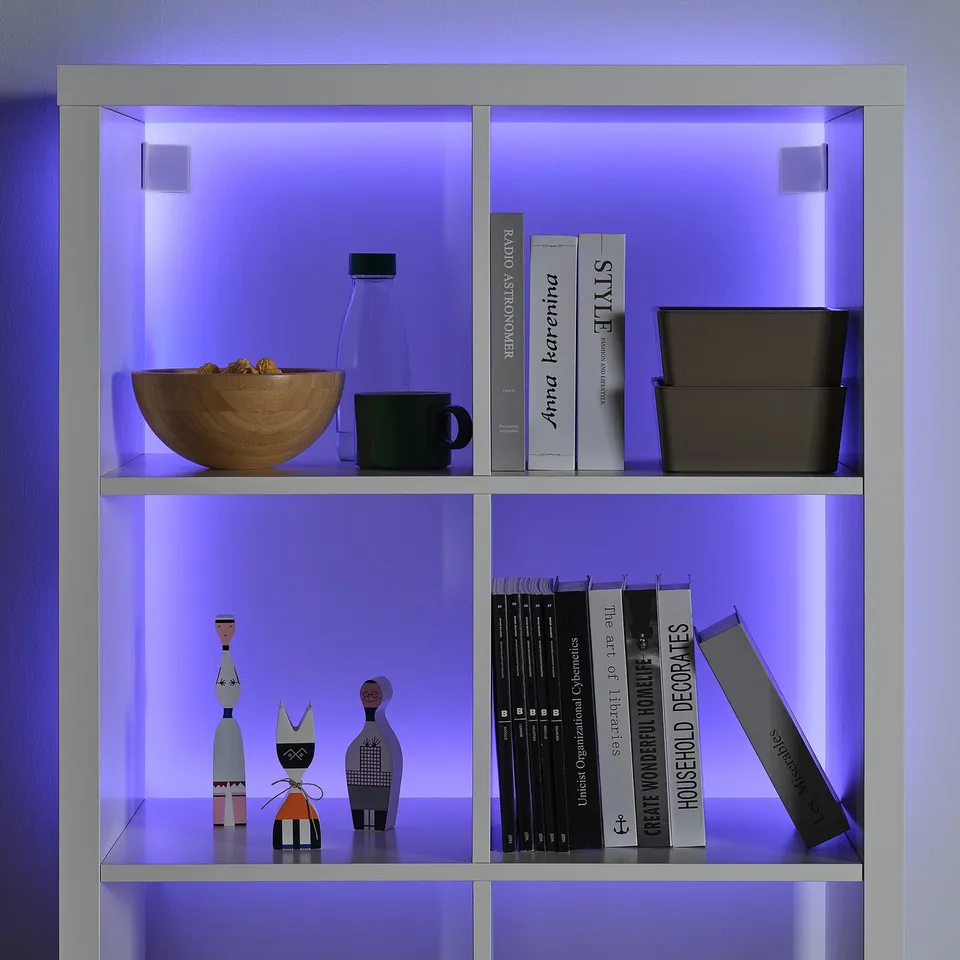 Led-lit shelf with blue light. Books, bowl, mug, vases, and decorations. Bright, modern design.