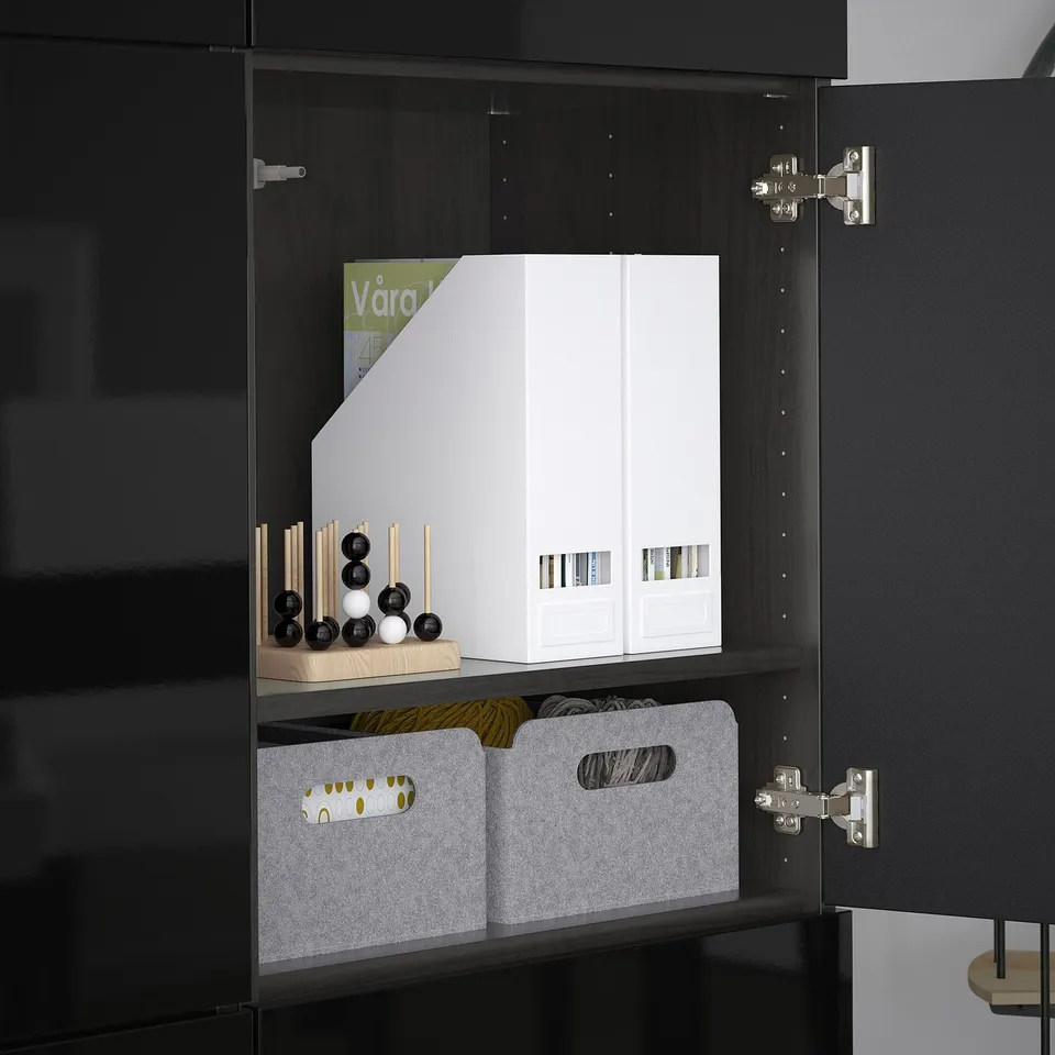 Black cabinet with adjustable shelves. It holds white storage boxes, grey bins, and decorative items. Hinges allow door adjustments.