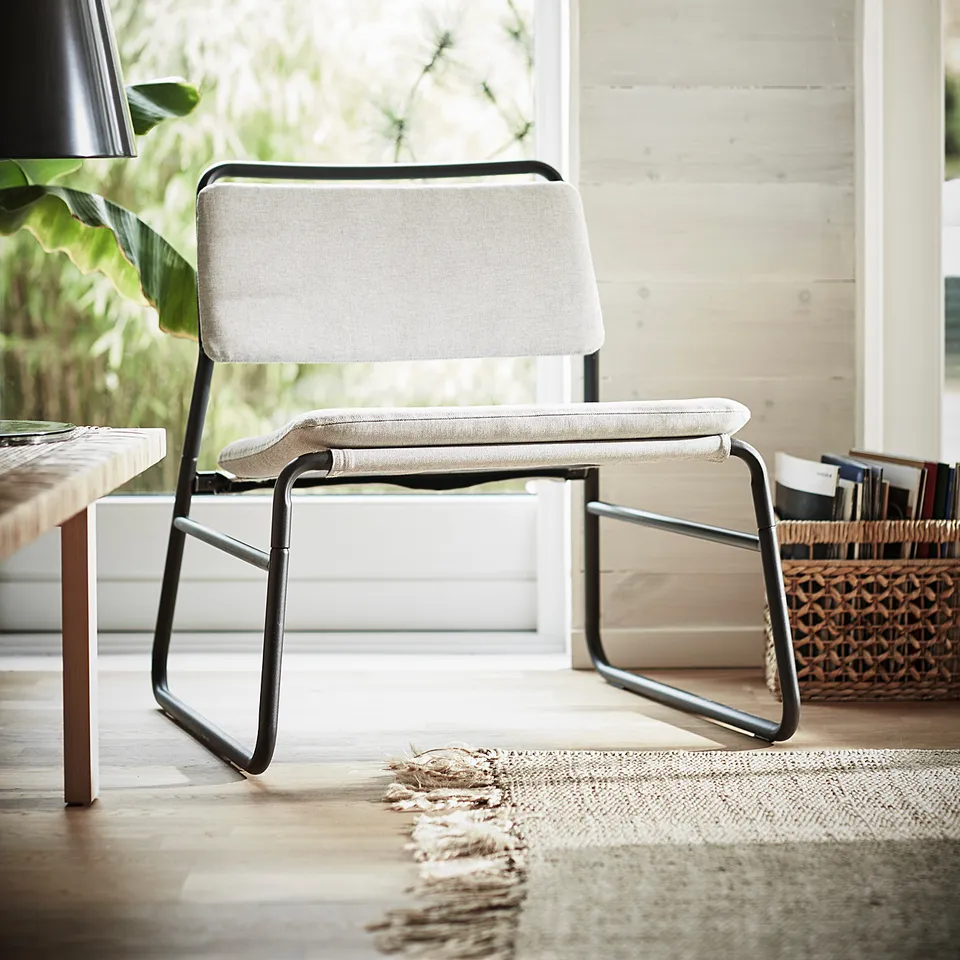 Modern beige easy chair with metal frame, soft cushions, near a window, exuding calm simplicity.