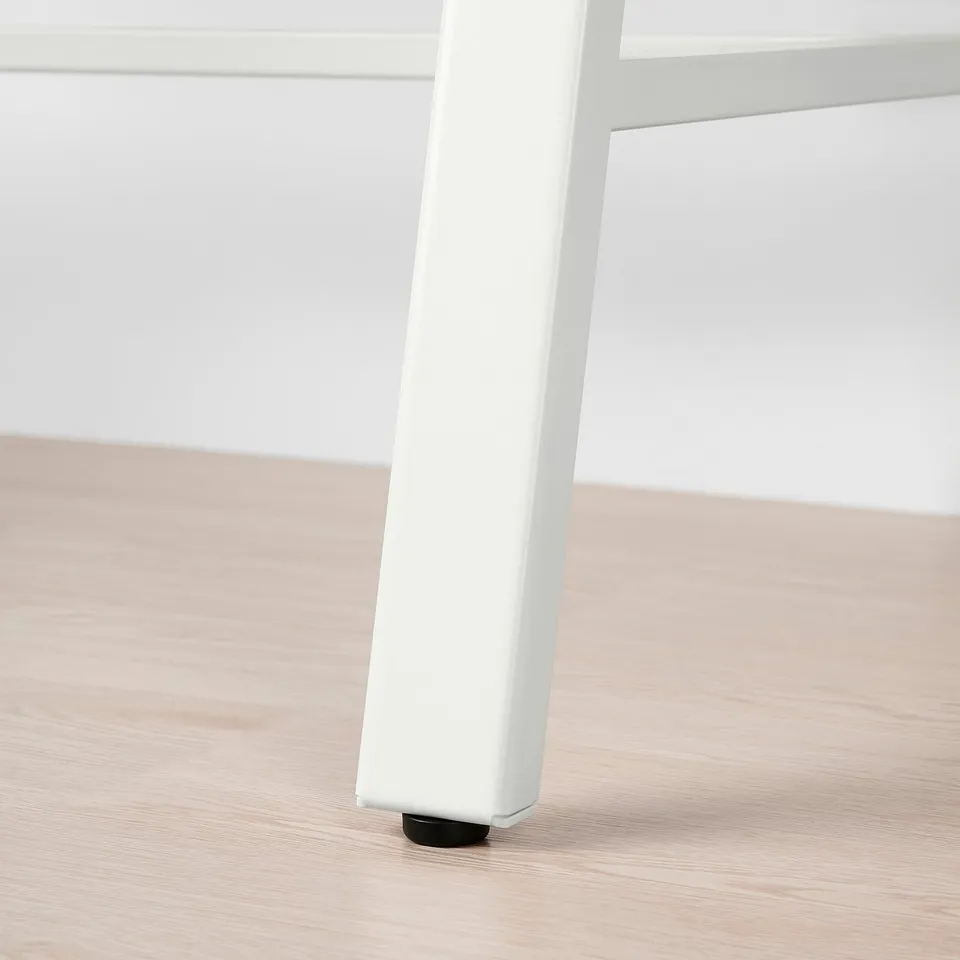 Close-up of a white adjustable desk leg with black floor protector, on light wooden floor.