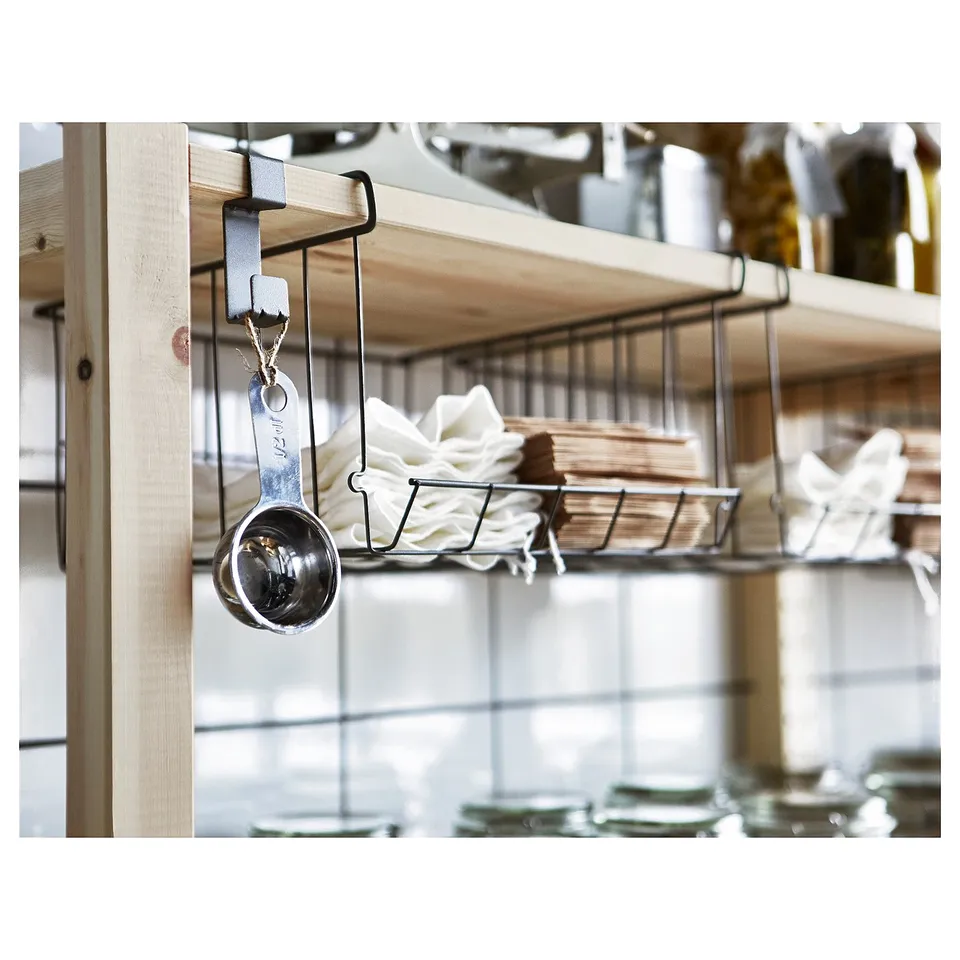 Silver steel measuring cup hangs from black metal hook, multiple shelves with white items in background.