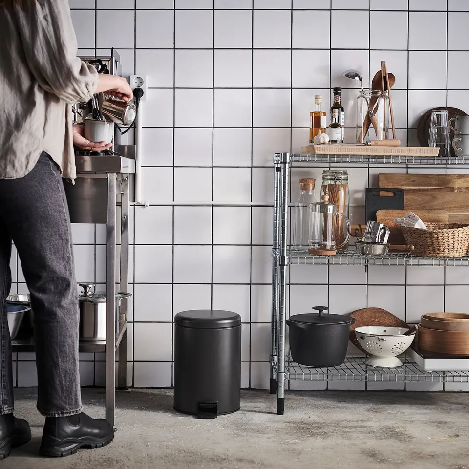 Person operates coffee machine in modern kitchen with metallic accents and organised shelves.