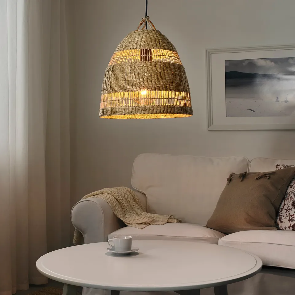 Hanging lamp TORARED made of seagrass, emitting warm glow over coffee table and sofa.