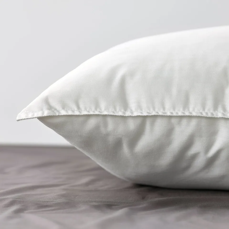 Close-up of a soft, white pillow with smooth cotton cover, folded on a bed, showcasing its comfort and quality.