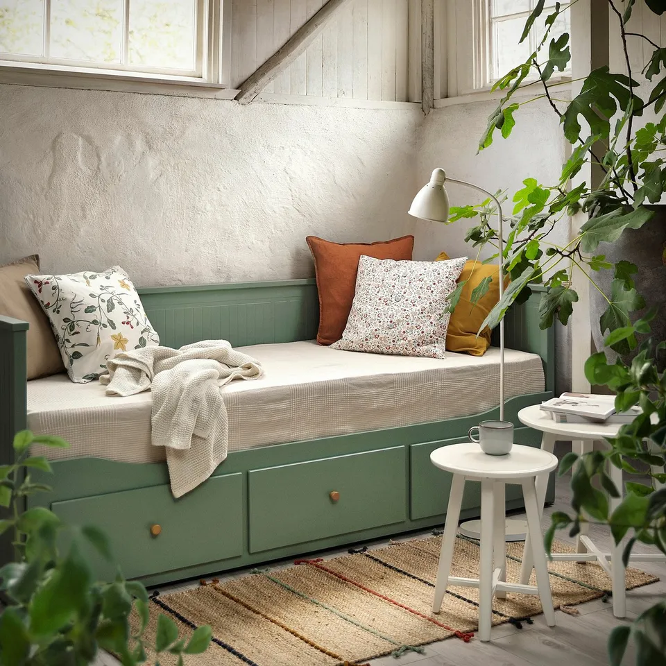 Cosy green day-bed with storage, comfort mat, and cushions. Perfect for small spaces, fits under windows. Decorated with pillows and plants.