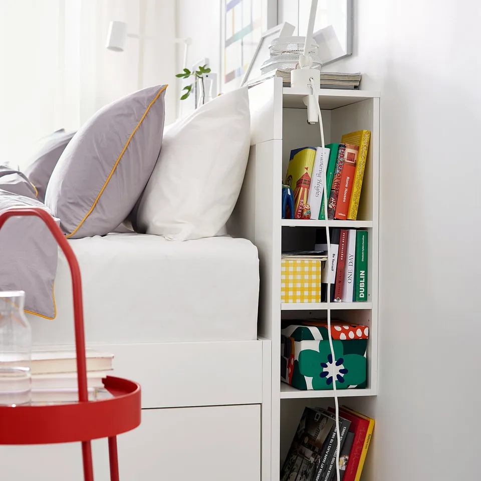 Bedroom with white BRIMNES bed, purple pillows, and colourful books on shelf.