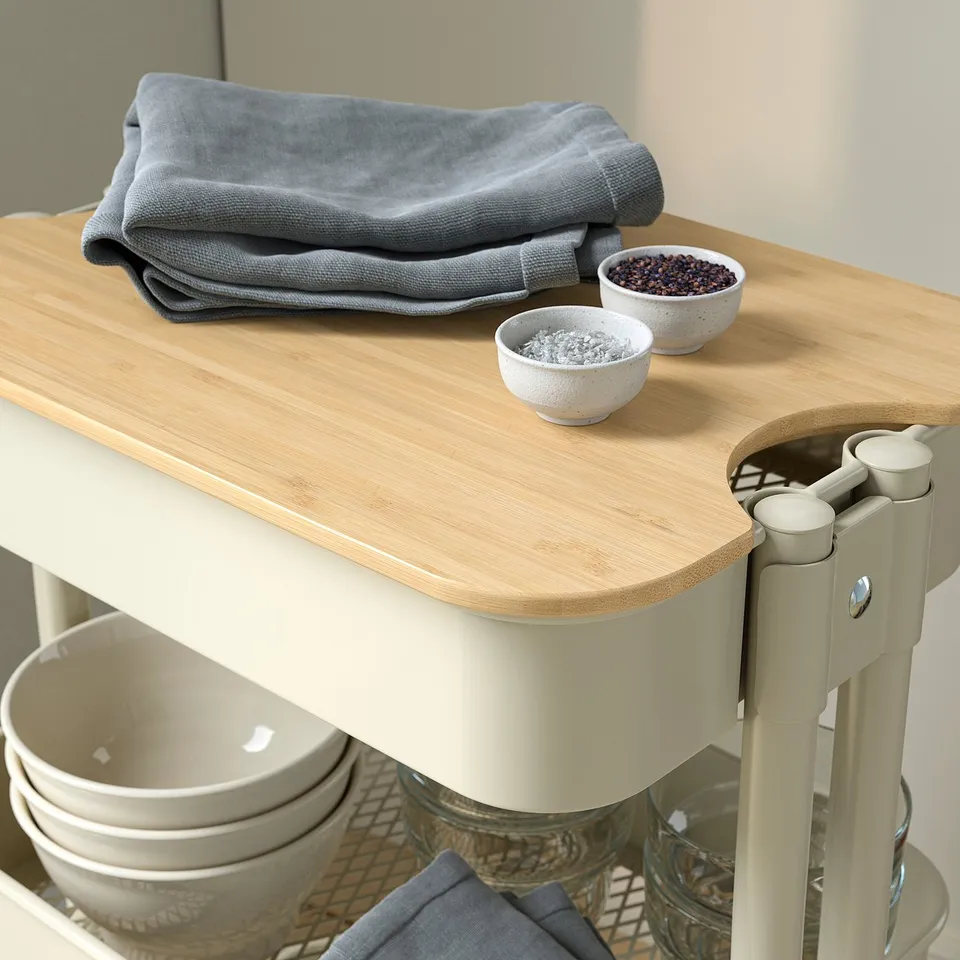 Wooden-topped trolley with stackable bowls, neatly folded grey cloths, sturdy cream legs, and baskets for storage.
