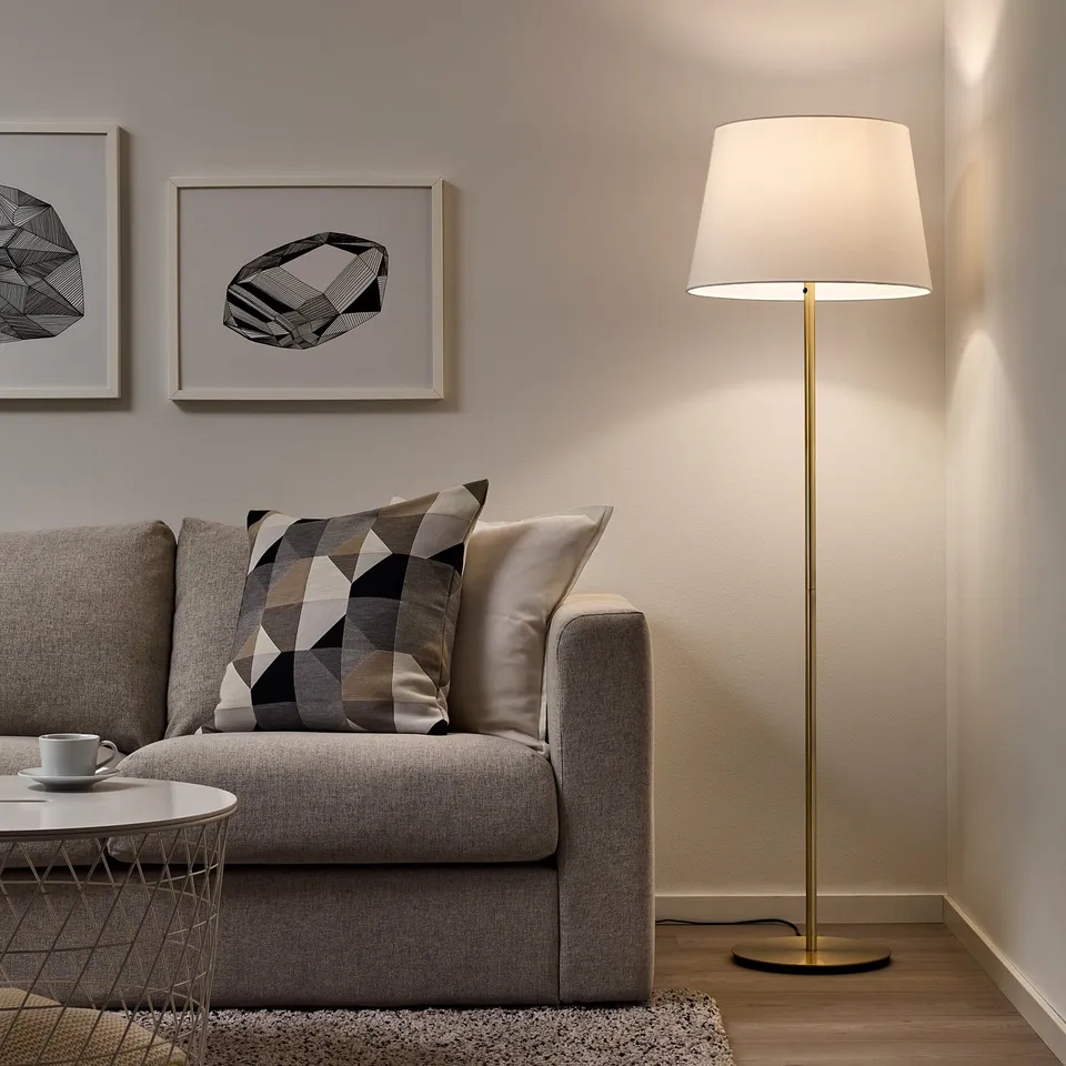 Modern living room with grey sofa, patterned pillow, coffee table, and tall floor lamp with white shade in corner, providing cosy light.