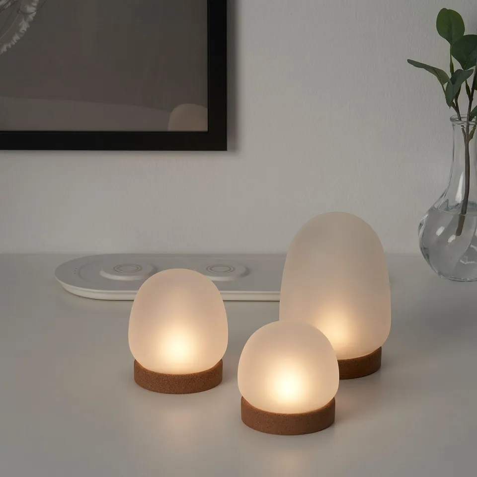 Three frosted glass lamps emit warm, flickering candle-like light and charge via micro-usb on a sleek tray.