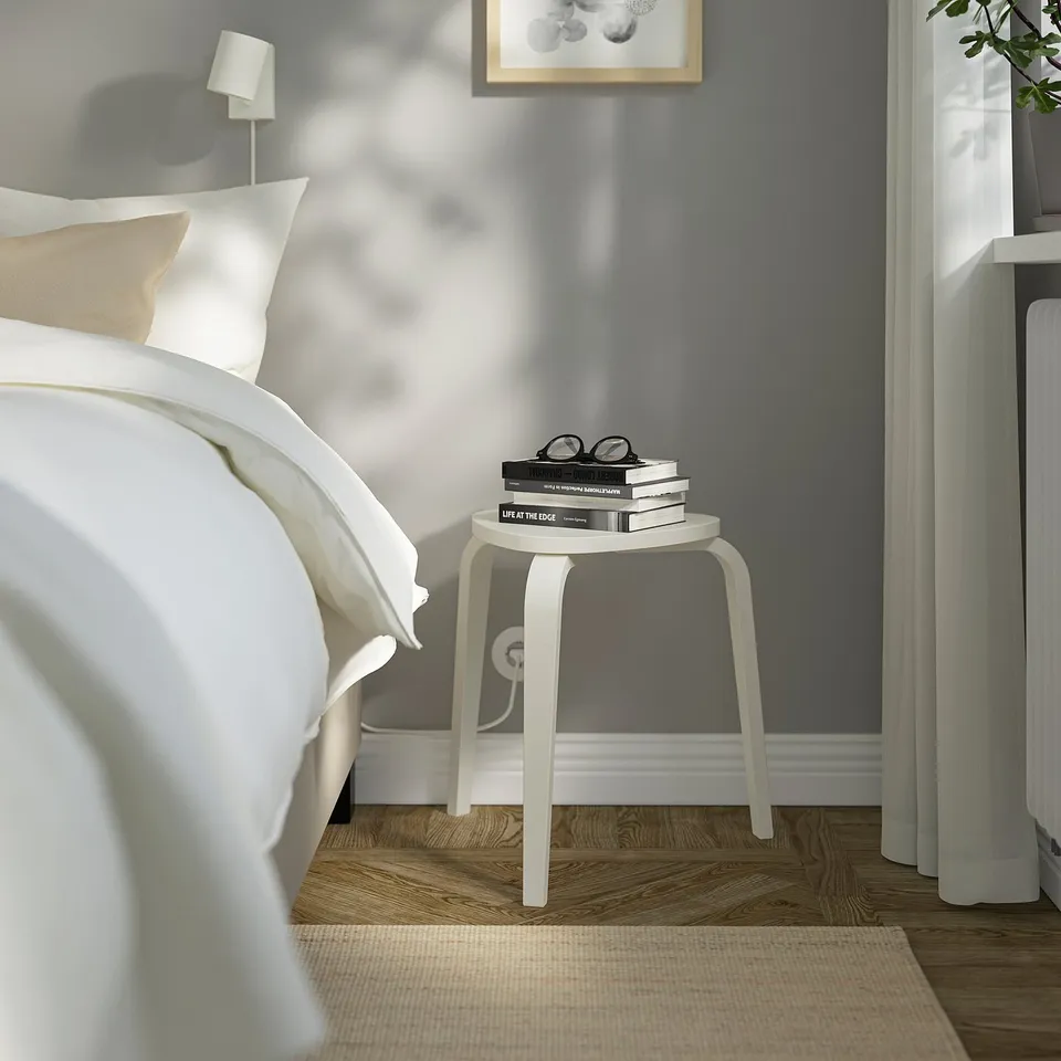 KYRRE stool beside bed, holding books; birch veneer, triangular seat.