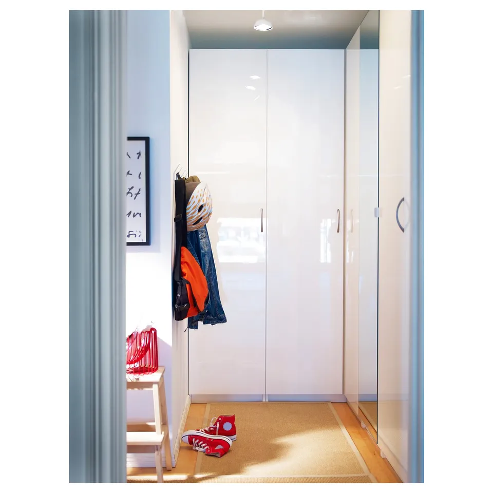 A modern, white glossy FARDAL door with minimalist design, a coat hook, and a small chair with red items.