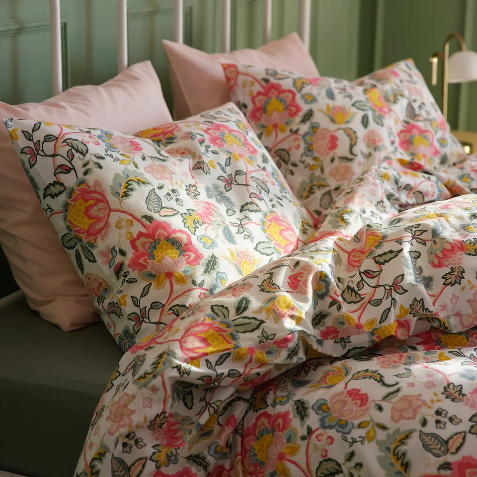 Flowery bedding set with pink, red, and yellow patterns on white. Green bed, durable, comfortable.
