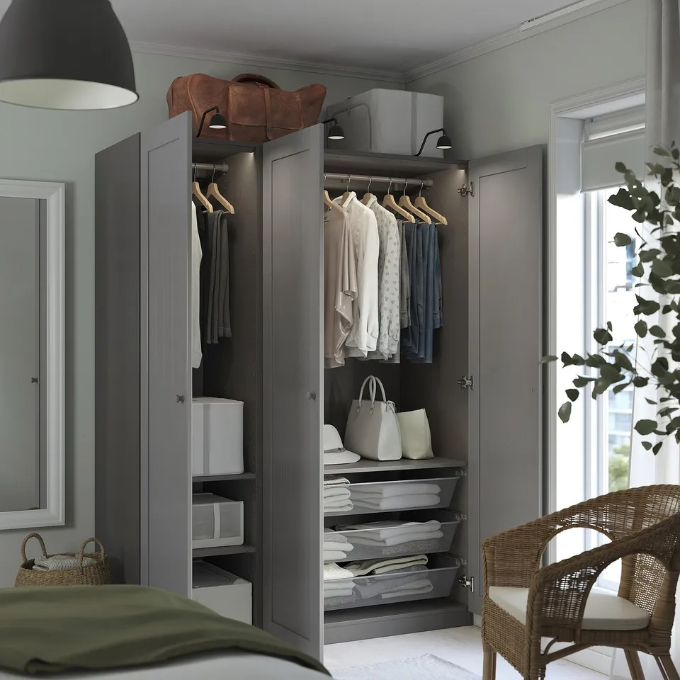 Modern closet with open doors revealing clothes on hangers, folded items, and shelves, positioned near a window with a wicker chair and plant.