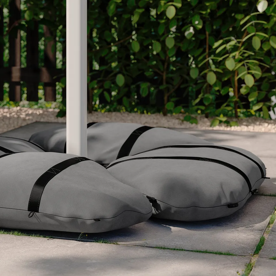 Two grey portable outdoor cushions lay on a concrete surface near greenery. They have black straps and zippers for easy carrying and storage.