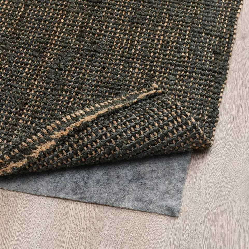 Dark green jute rug folded on wooden floor, with grey underlay for stability and comfort.