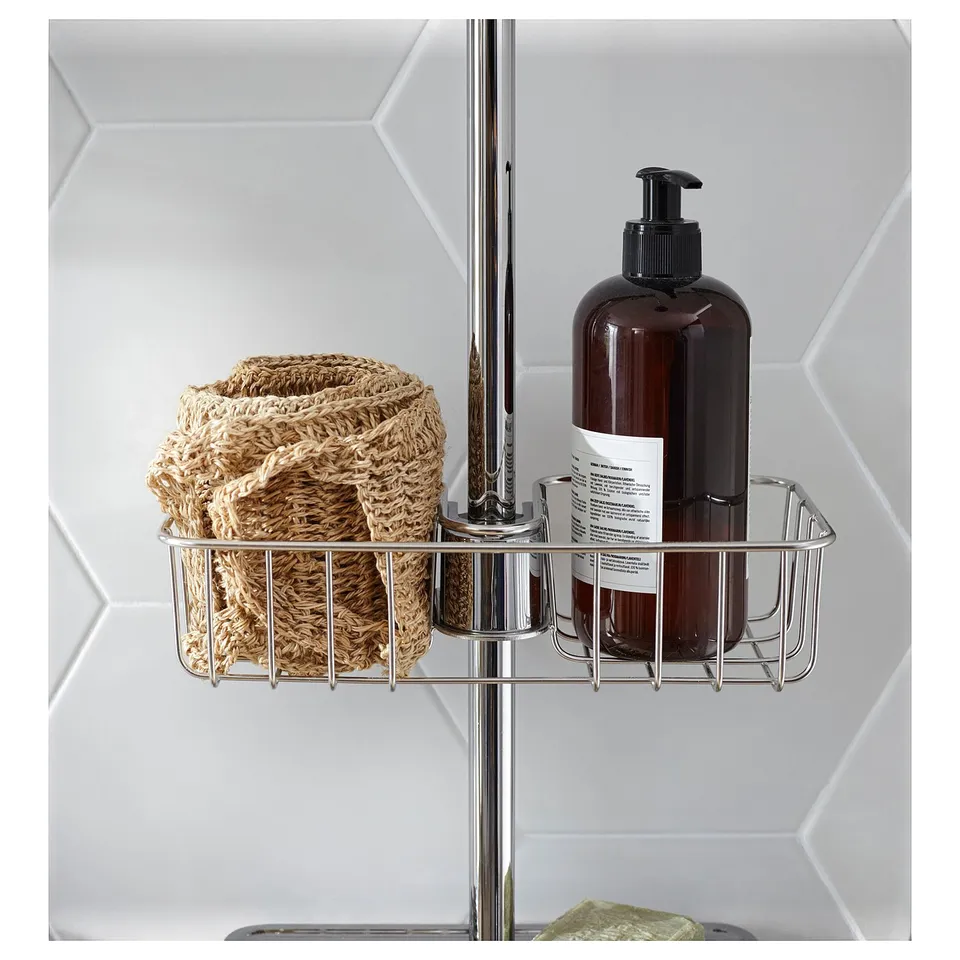 A chrome VOXNAN shower basket with a brown soap dispenser, mounted on a metal pole. The basket holds natural-looking woven items.