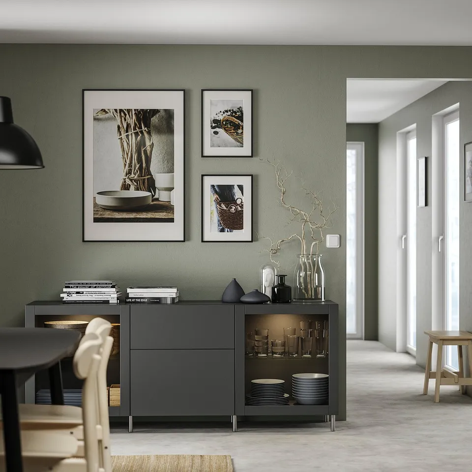 Modern dining room with dark grey BESTÅ sideboard, green walls, black pendant light, wooden chairs, and glassware.