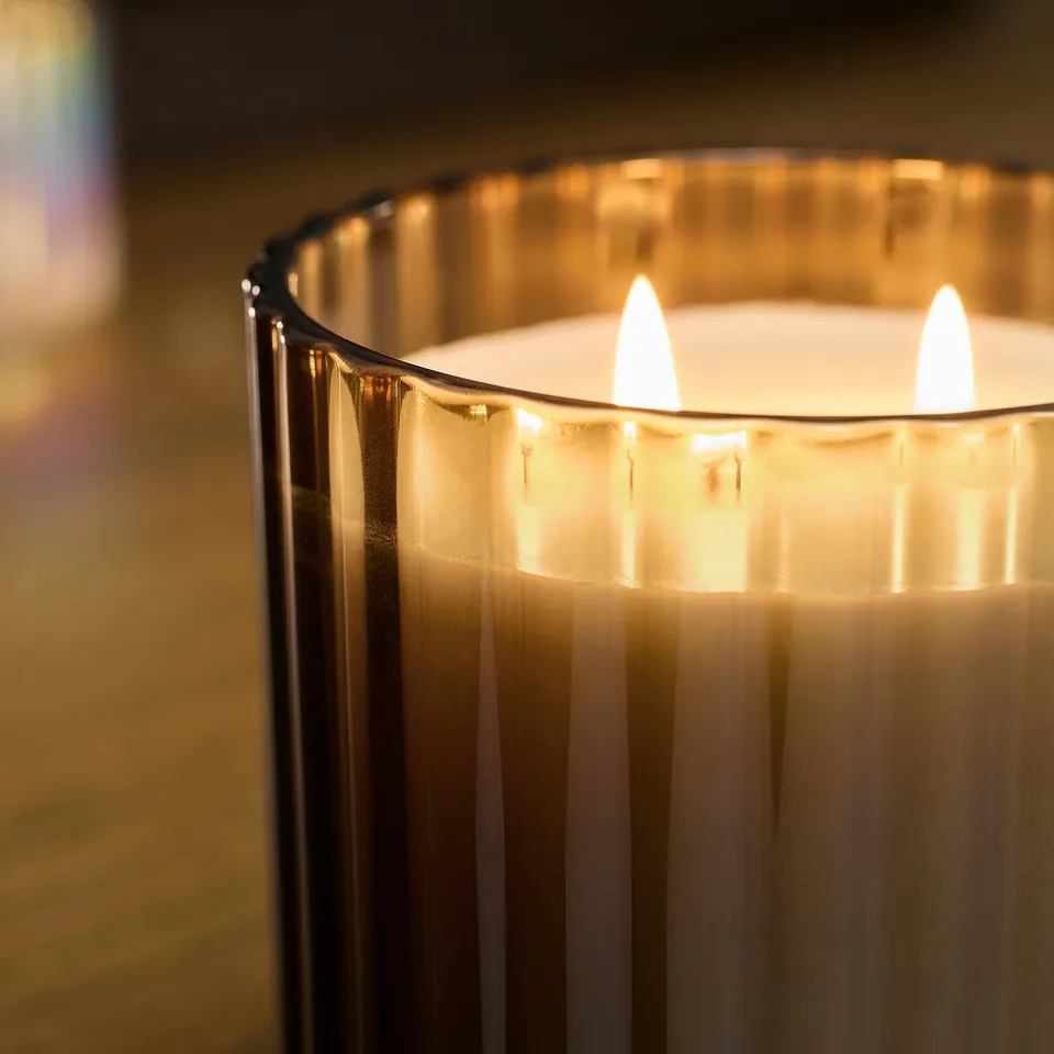 A lit 3-wick scented candle in a glass container, emitting a warm, inviting glow and filling the room with a calming natural scent.
