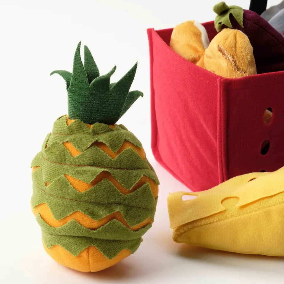 Plush pineapple toy beside fabric shopping basket with vegetables. High-quality materials, vibrant colours, detailed design.