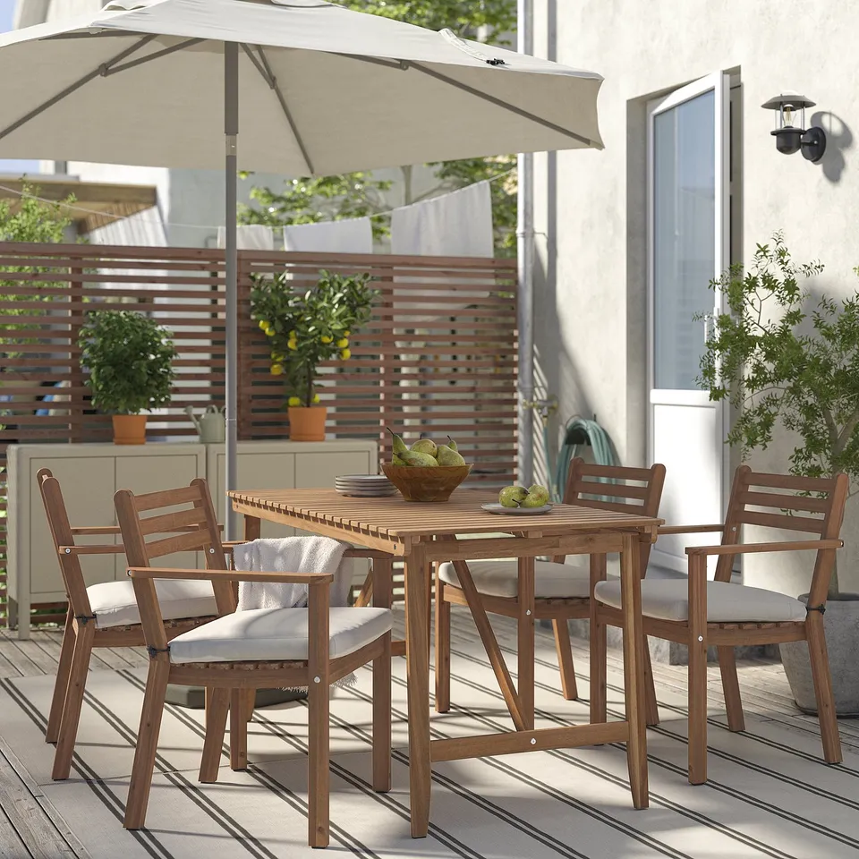 ASKHOLMEN: brown acacia table & 4 chairs on deck. Large potted plants, umbrella, bowl of fruit, rug, greenery. Modern, cosy, outdoor dining set.
